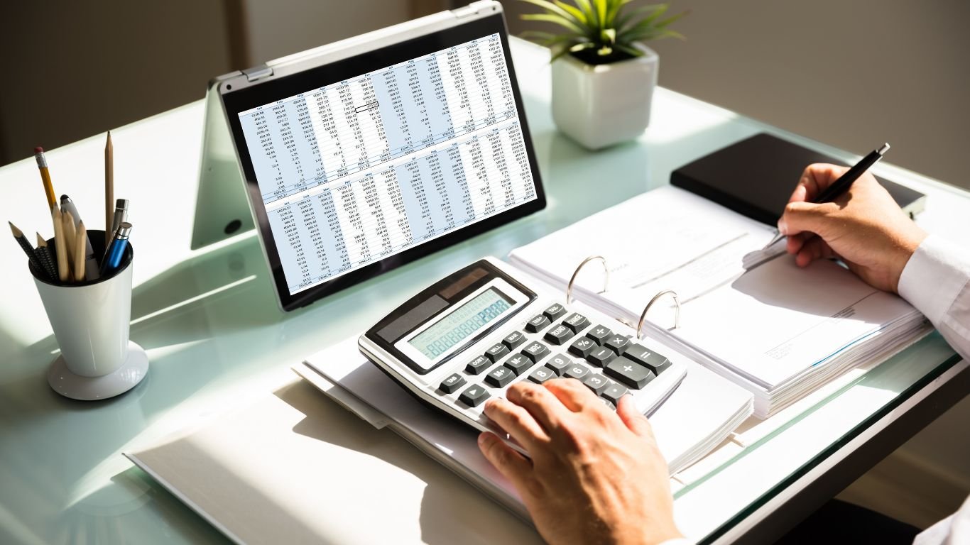 Mesa de escritório com laptop, planilhas e calculadora durante análise contábil